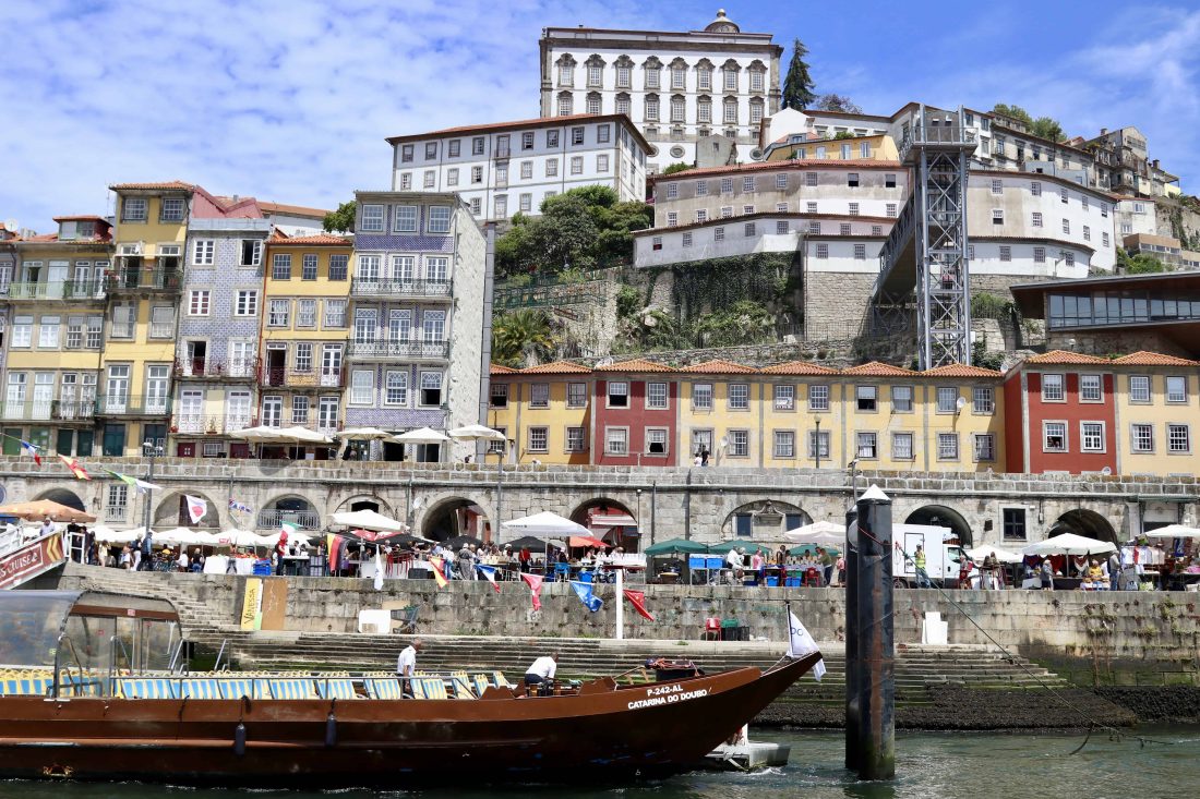 View from the boat tour on the Douro River with the waterfront and colorful houses in front of the hill where the Porto Cathedral is located.