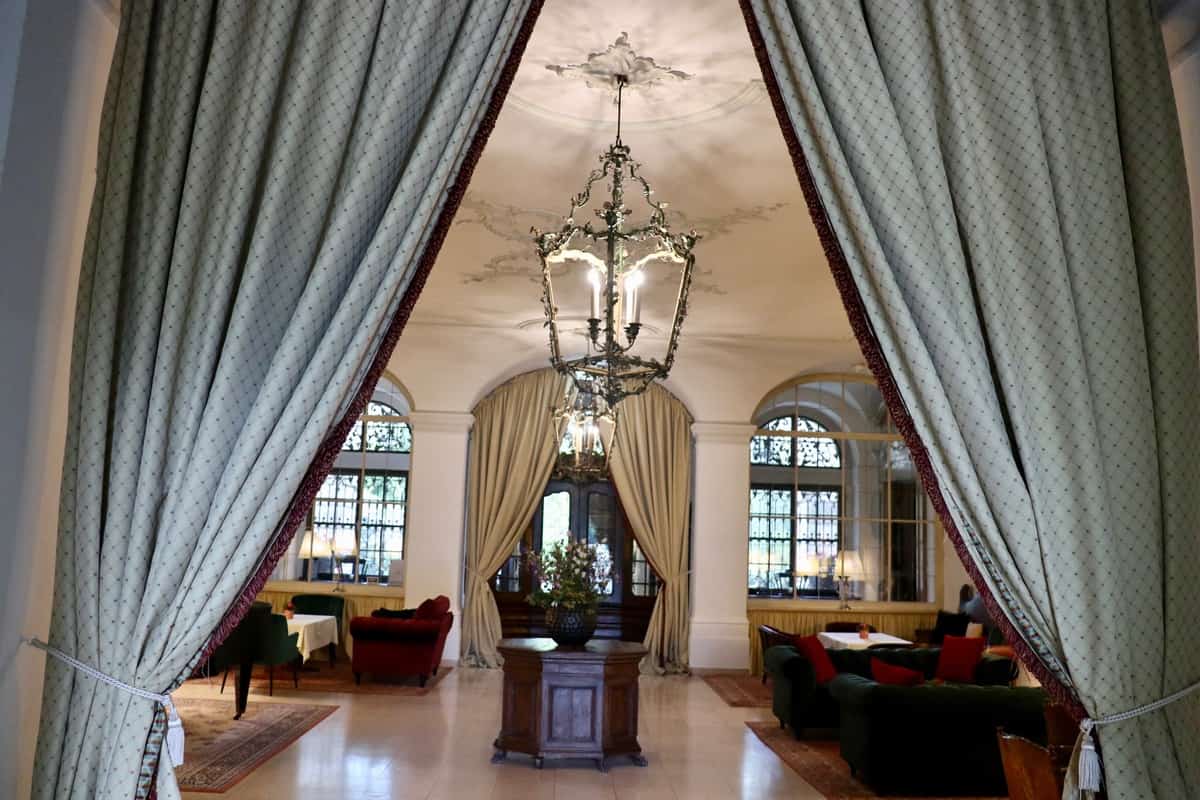 An open curtain gives a view of the Great Hall with a chandelier, a marble floor, and seating areas.