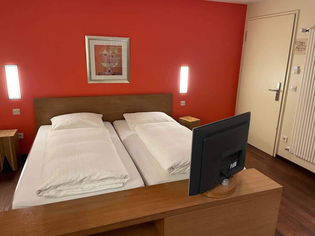 gemütliches Doppelzimmer mit roter Wand, sowie TV am Fußendes des Bettes im Hotel Schwan in Wertheim.