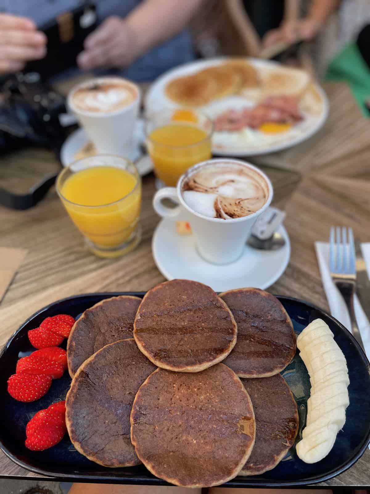 Pfannkuchen mit Banane und Erdbeeren und Cappuccino bei einem Frühstück am Place Rossetti in der Nizza Altstadt
