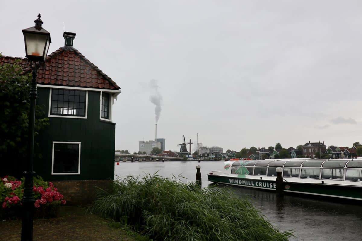 Ufer der Zaan mit buntem Holzhaus und dem Schiff, welches eine Rundfahrt zu den Windmühlen führt.