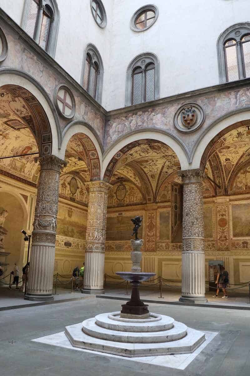 Blick auf den mit Säulen und Fresken verzierten Innenhof und die Statue Putte mit Delfin im Palazzo Vecchio