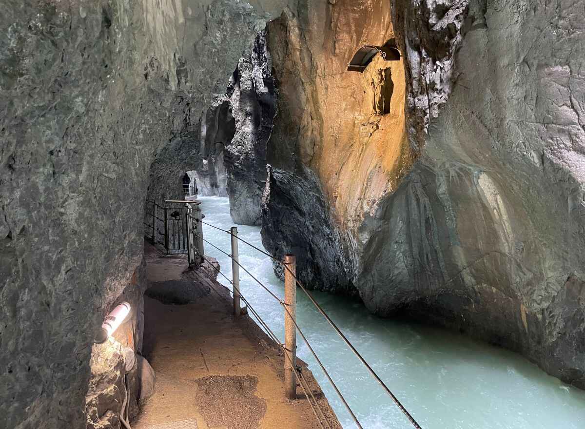 View of the stunning Partnachklamm Gorge in Garmisch-Partenkirchen, with the narrow path alongside the turquoise river, surrounded by impressive rock walls, is one of the top attractions near Neuschwanstein Castle.