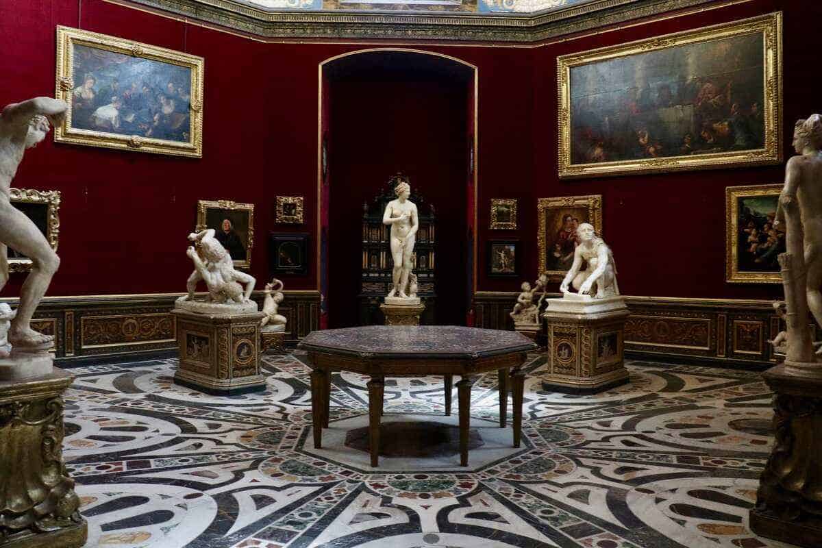 Blick auf einen der Räume mit Skulpturen aus weißem Marmor und mit Goldrahmen eingefassten Gemälden in den Uffizien