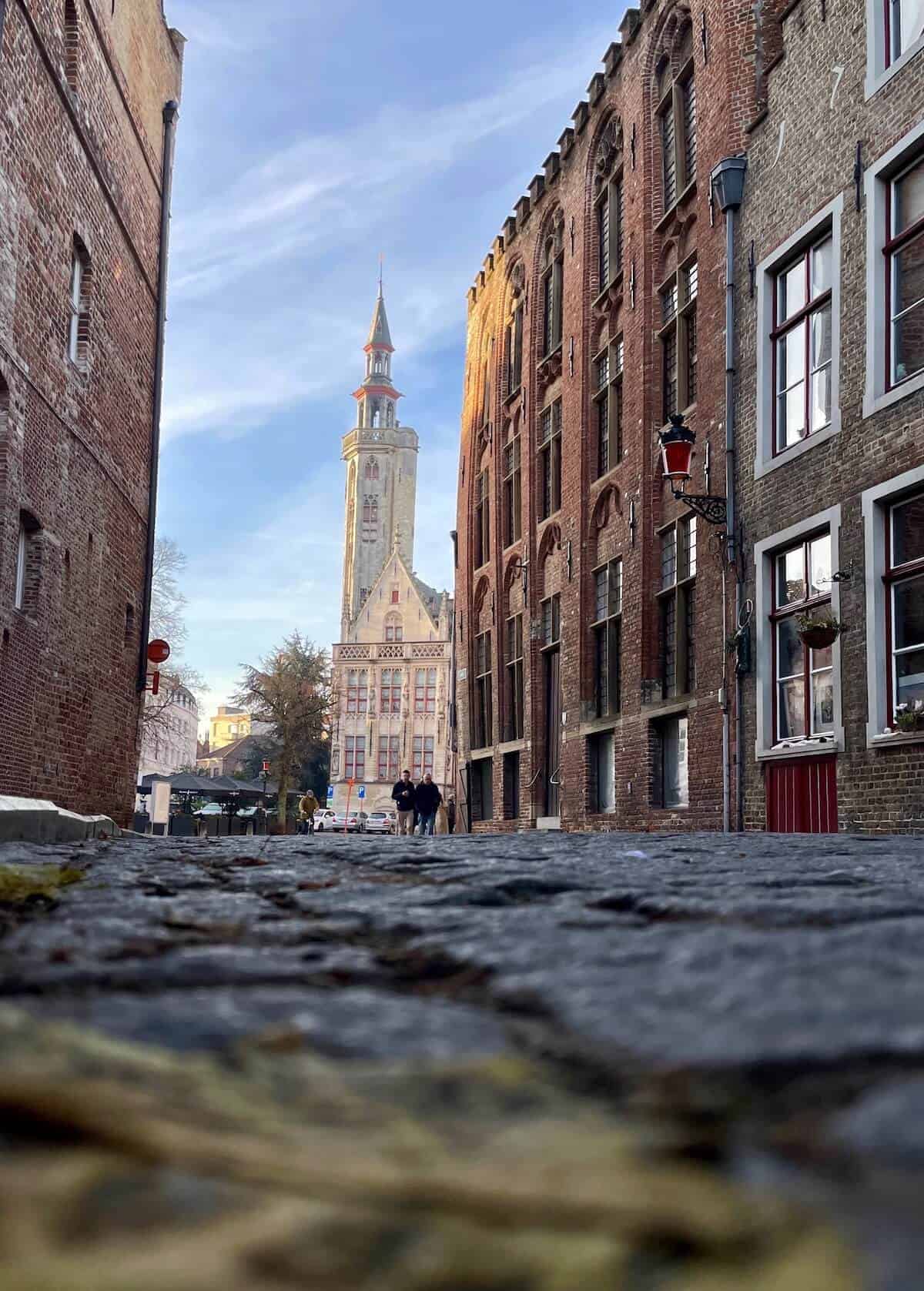 View of a narrow, cobblestoned alley with old buildings and a tower in the background.
