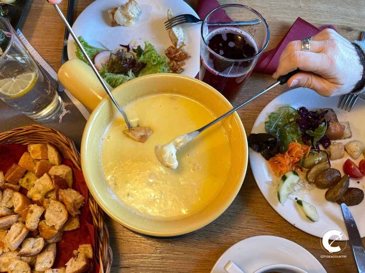 Tisch mit Käsefondue aus Tiroler Bergkäse und Zutaten wie Salat und Brotstücke auf der Aschinger Alm in Ebbs im Kufsteinerland