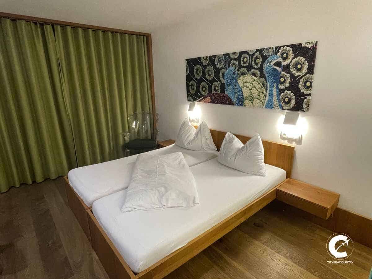 Zimmer im Hotel Sattlerwirt mit Holzboden, weißer Bettwäsche und grünem Vorhang