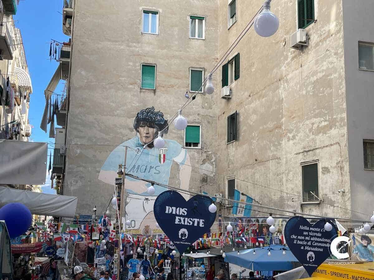 Haus aus Beton mit großem Mural von Diego Maradona und Ständen mit Souvenirs im Vordergrund.
