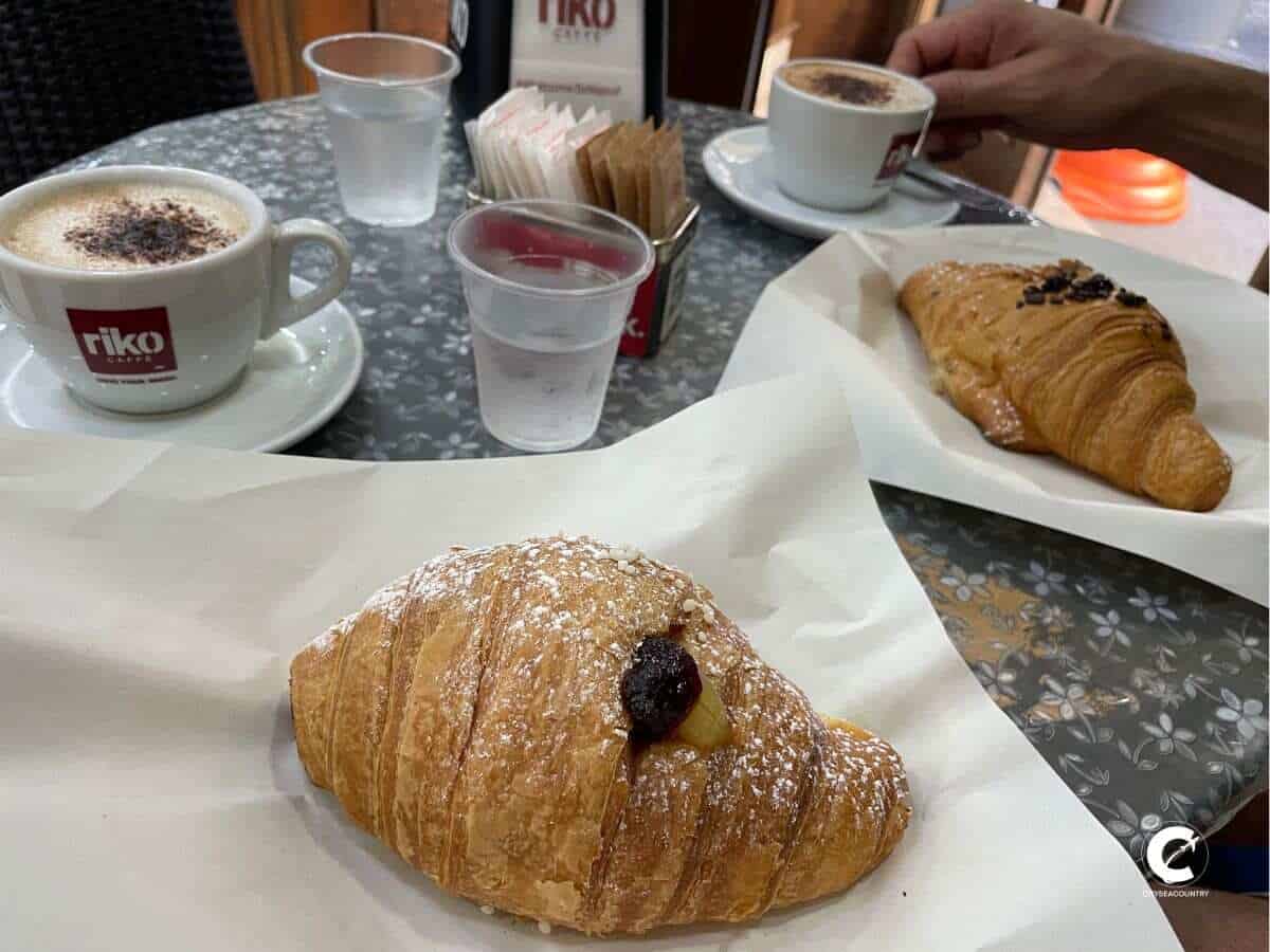 Frückstück in Neapel mit süßem Gebäck im Vordergrund und Cappuccino im Hintergrund.