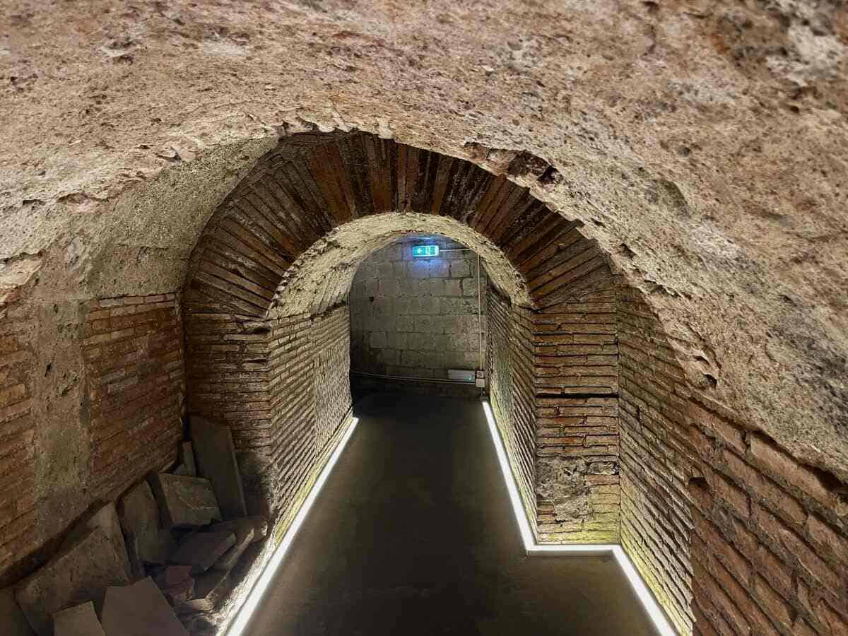 Unterirdischer, beleuchteter Tunnel mit Rundbögen aus Ziegelsteinen, welcher durch das Labyrinth im Untergrund von Neapel führt.