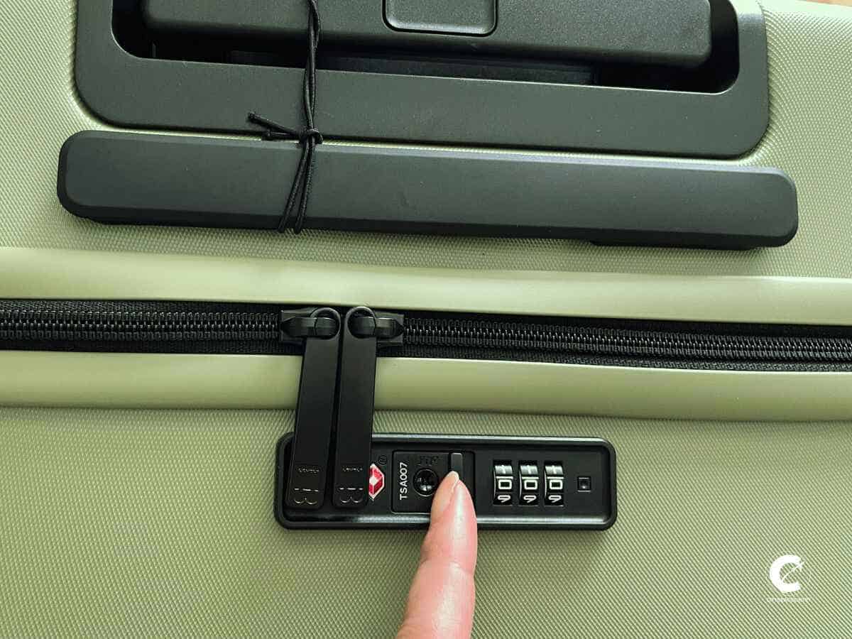 View of the exterior of the Level8 Luminous Textured 20'' in olivine color with a finger pointing on the integrated TSA-approved lock.