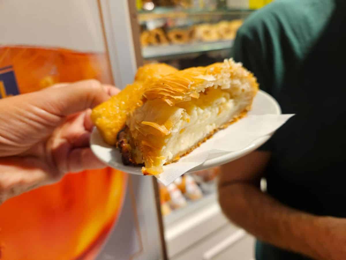 Sfogliatella mit den typischen dünnen, gefalteten Teigblättern und einer süßen Füllung auf einem Papierteller vor einer Bäckerei in Neapel.