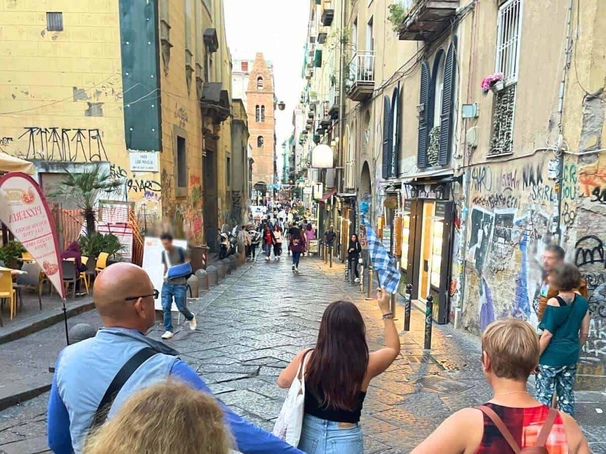 Straße in der Altstadt von Neapel mit Guide mit blau-weiß gestreifter Fahne, die die Street Food Tour begleitet