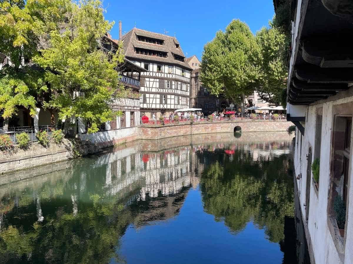 Blick auf den gemächlich fließenden dunklen Fluss mit Spiegelung eines Fachwerkhauses im Wasser in Petite France in Strasbourg