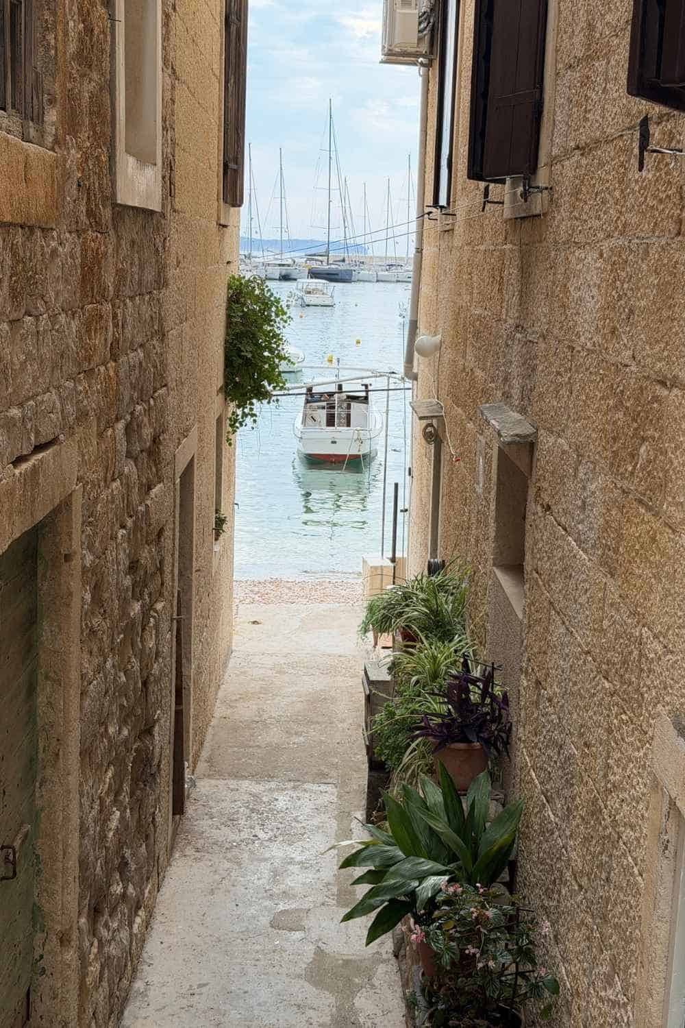 Gasse in Komiza mit Blick auf ein Schiff und das hellblaue Wasser auf der Insel Vis