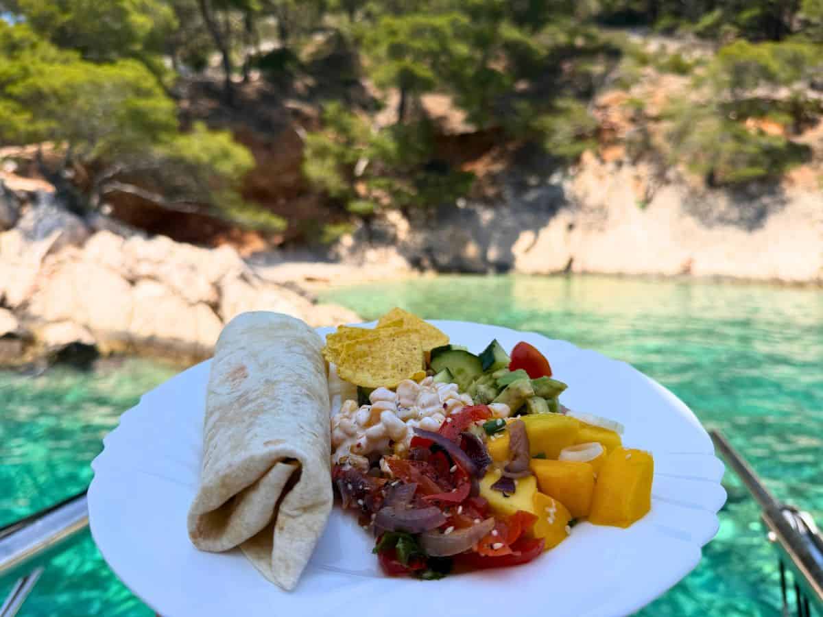 Teller mit Wrap, Salat und Gemüse vor türkisfarbener Bucht und kleiner Insel in Kroatien
