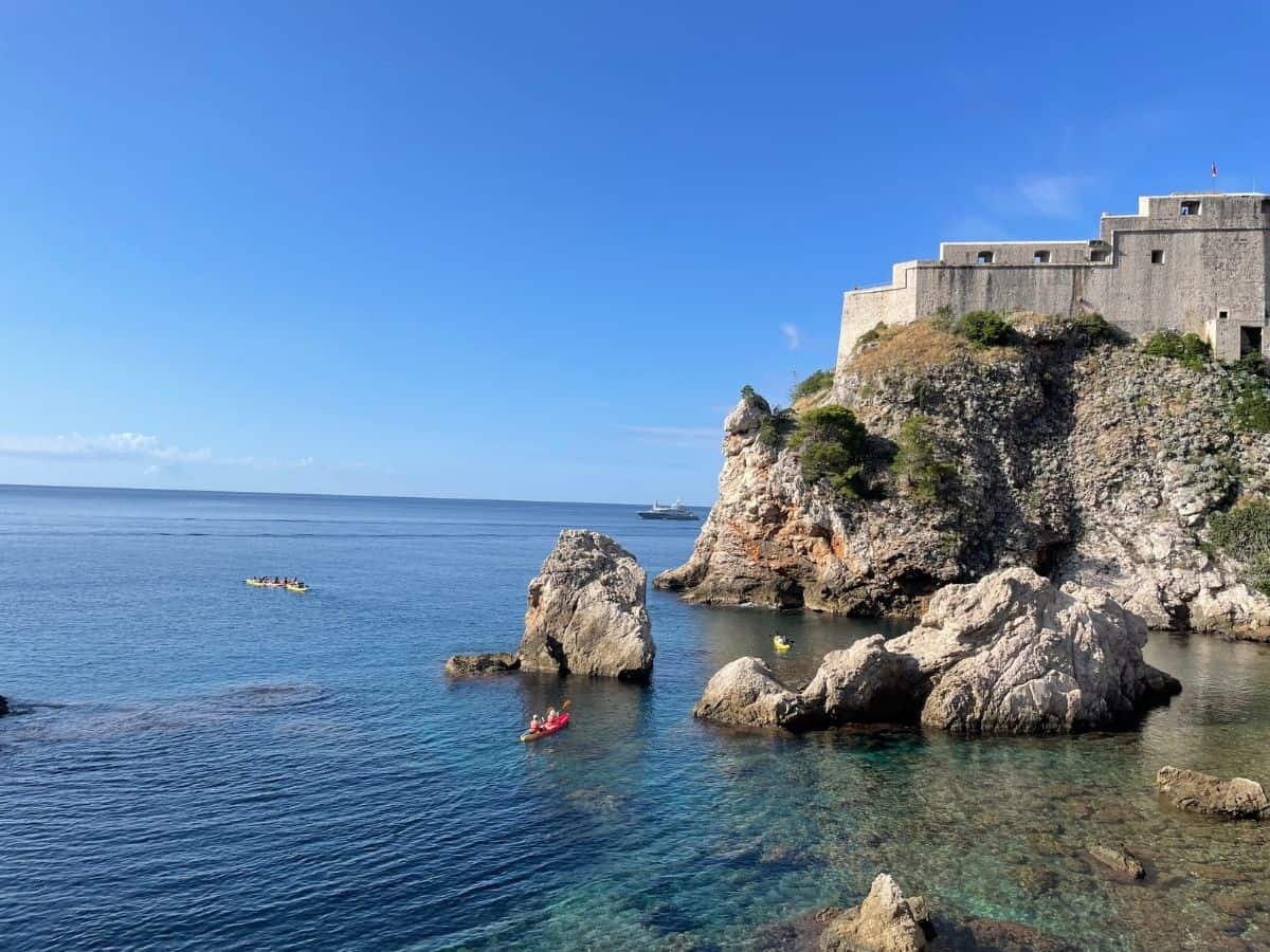Klippen mit Festung am Meer und Kajakfahrern bei ruhigem klaren Meer