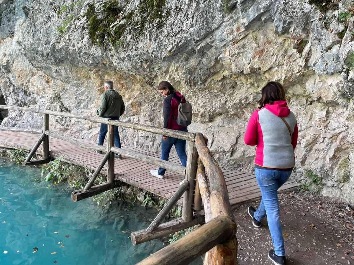 Wandersteg unter einem Felsen neben dem Wasser mit drei Wanderern